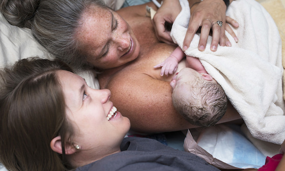 Woman who has just given birth holding new baby while another smiling woman looks on