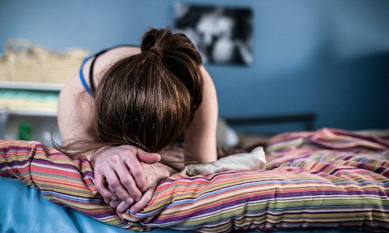 Woman feeling hopeless and lost with head on hands on bed